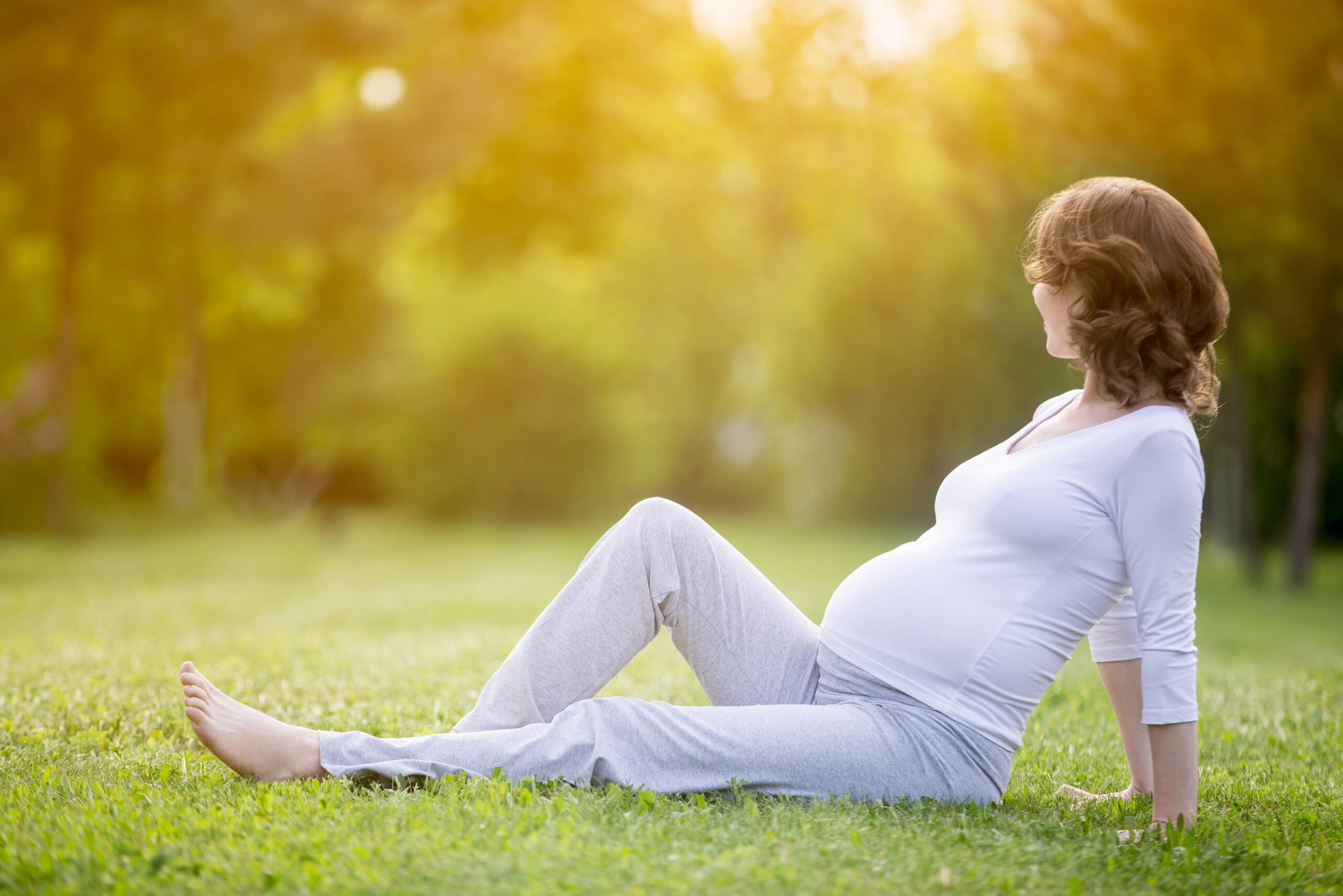 Happy pregnant woman on late pregnancy stage sitting on grass la